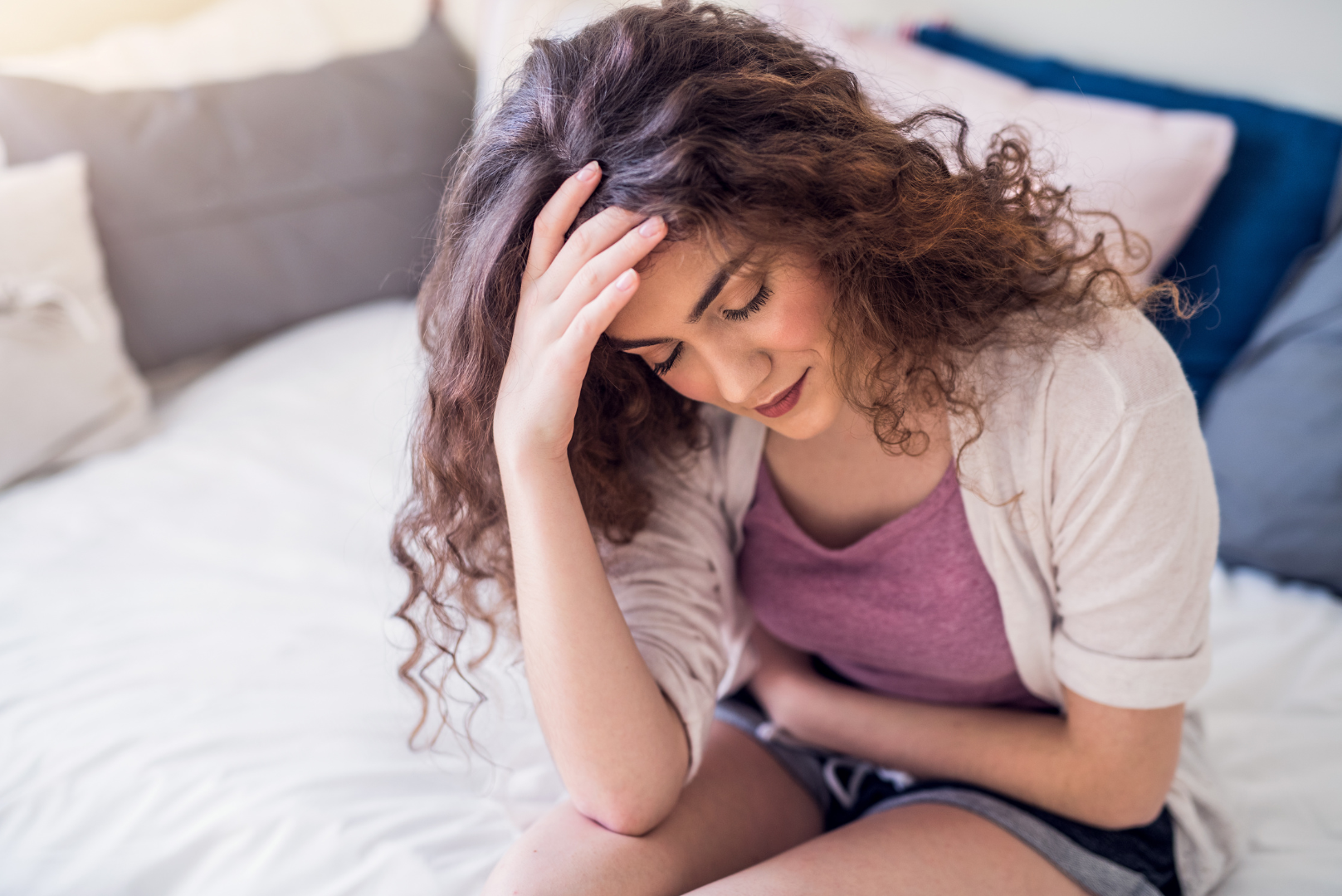 Young woman sitting on a bed holding her abdomen