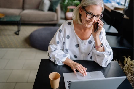 A woman smiling while talking on the phone at her laptop