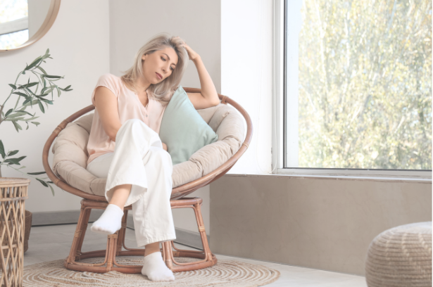 Woman resting in a papasan chair, holding her head with a headache